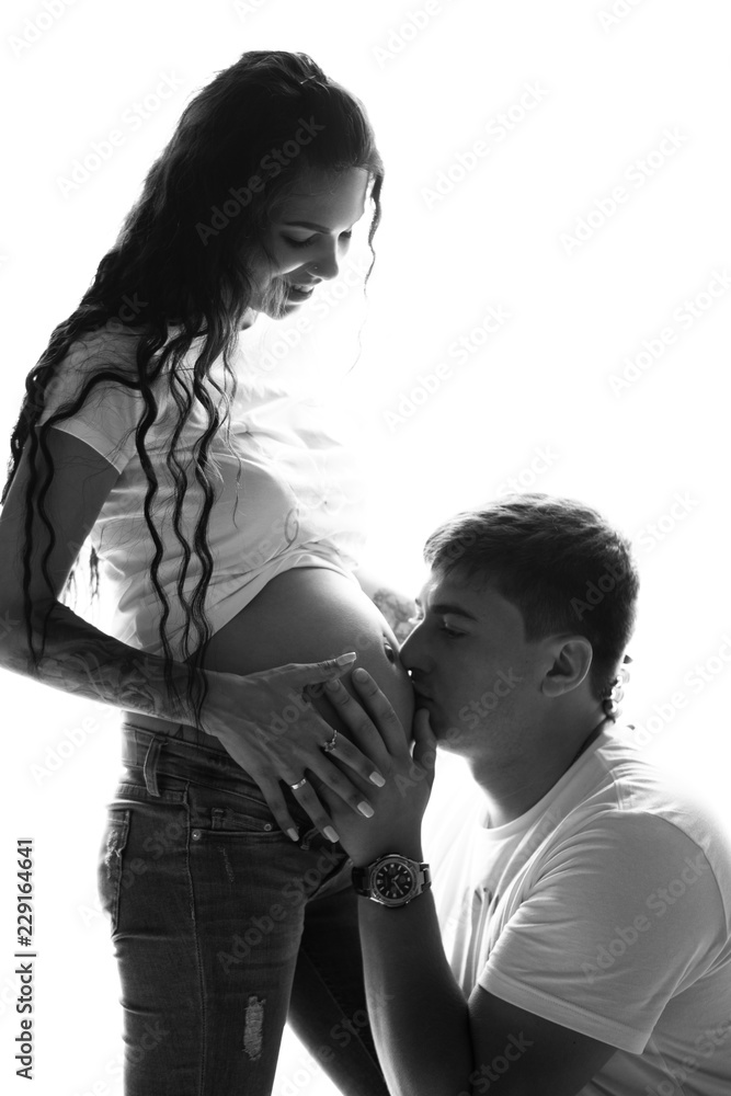 Portrait of cheerful married and pregnant couple spending time together at home. Future dad kissing belly of his pregnant wife - black and white image Portrait of cheerful married and pregnant couple spending time together at home. Future dad kissing belly of his pregnant wife - black and white image