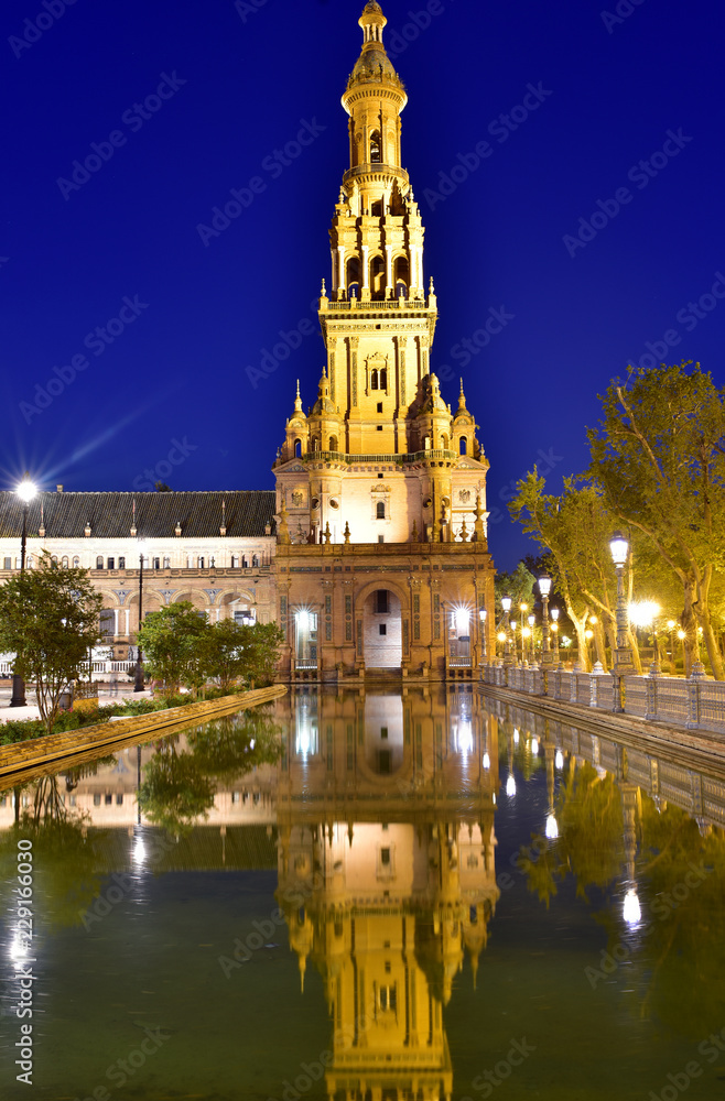 Tower reflected in water basin, illuminated Plaza de Espana, night view, Seville, Andalusia, Spain