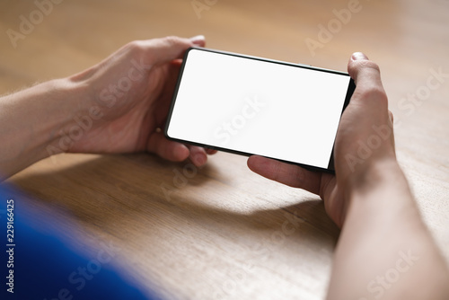 Fototapeta Naklejka Na Ścianę i Meble -  young man hands holding smartphone with blank white screen in landscape mode