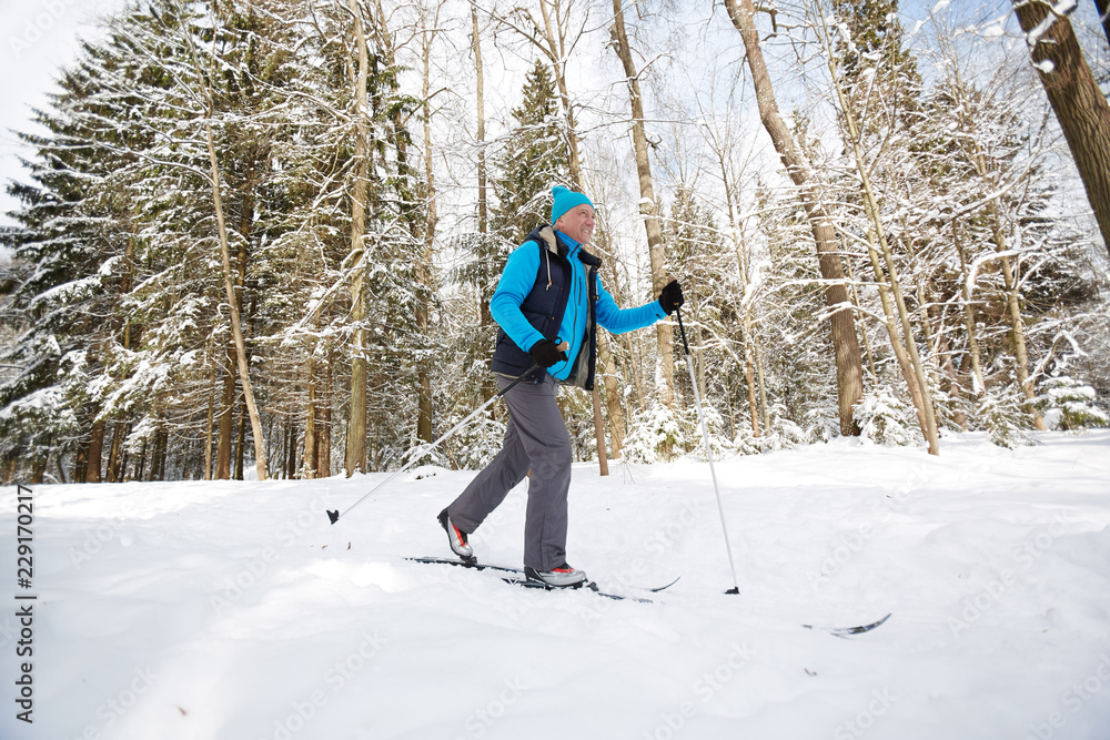 Aged active sportsman skiing down ski track in winter forest on frosty day or weekend