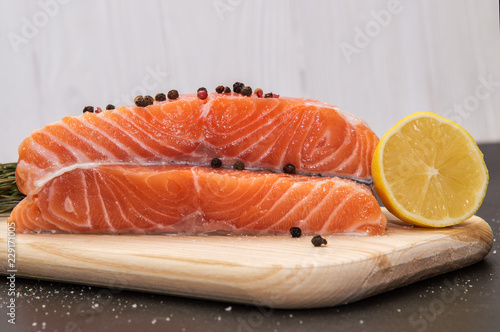 Close up. Ingredients. Fresh salmon steak surrounded by lemon and spices on a wooden board. Black and white background.
