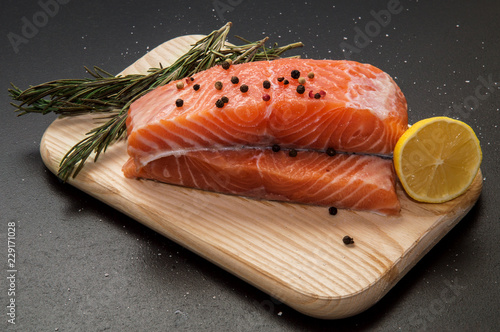 Close up. Ingredients. Fresh salmon steak surrounded by lemon, pepper and rosemary on a wooden board. Black background.