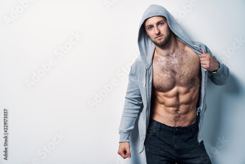 Photography Brutal naked muscular man dressed in a grey hoodie posing by white wall, looking
