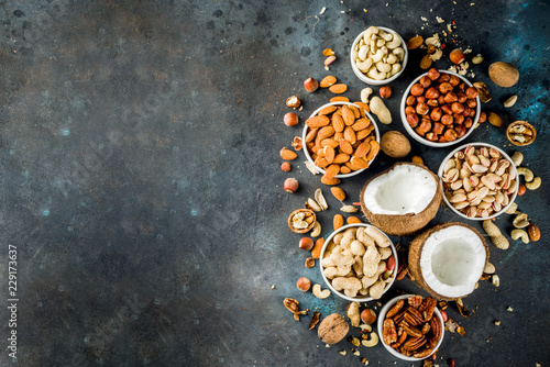 Various types of nuts - walnuts  pecans  peanuts  hazelnuts  coconut  almonds  cashews  in bowls  on a dark blue concrete table top view