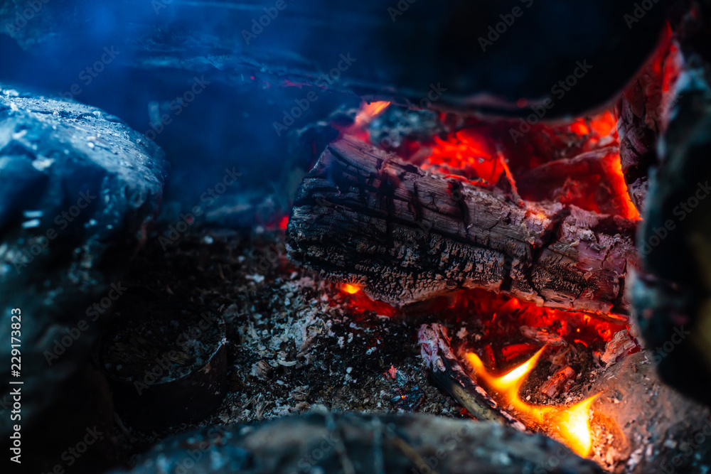 Smoldered logs burned in vivid fire. Atmospheric background with orange flame of campfire. Unimaginable detailed image of bonfire from inside with copy space. Smoke and ashes close up. Smoldered logs burned in vivid fire. Atmospheric background with orange flame of campfire. Unimaginable detailed image of bonfire from inside with copy space. Smoke and ashes close up.