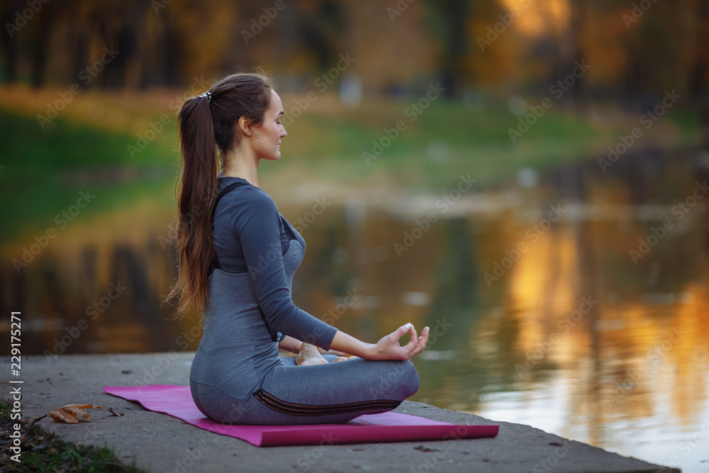 Young woman practicing yoga outdoors. Female meditate outdoor infront of beautiful autumn nature.
