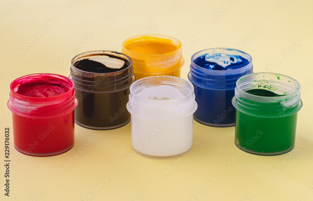 Jars with gouache on a yellow background. White, red, blue, green, brown paint. Jars with gouache on a yellow background. White, red, blue, green, brown paint.