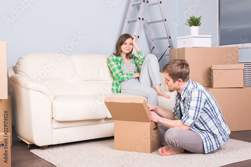 Moving, new apartment and relocation concept - Young man helping his wife with unpacking