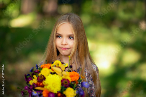 Portrait of Beautiful little girl with bouquet of autumn flowers in the park
