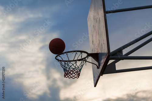 Basketball ball flies into the ring against the sky in the evening. © Elroi