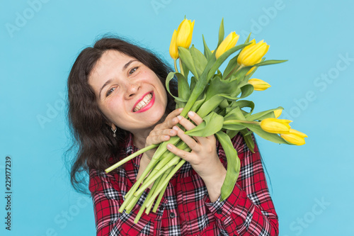 Close-up portrait of beautiful young woman with yellow tulips on blue background photo