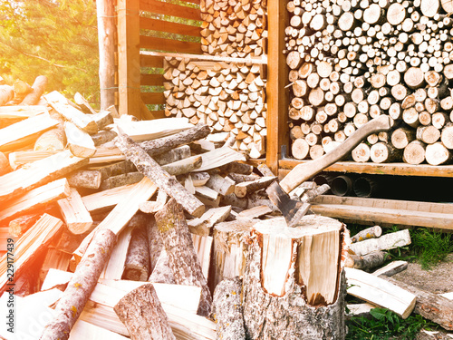 Punctured firewood in a pile, an ax in a stump against the background of a wood-burning barn