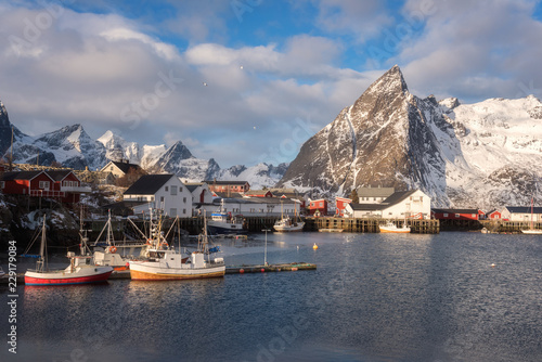 Scenic view of the small norwegian fishing village Hamnoy. Beautiful winter daytime landscape with boats, fjord, peaks of rocky mountains and blue cloudy sky on background, Lofoten Islands, Norway