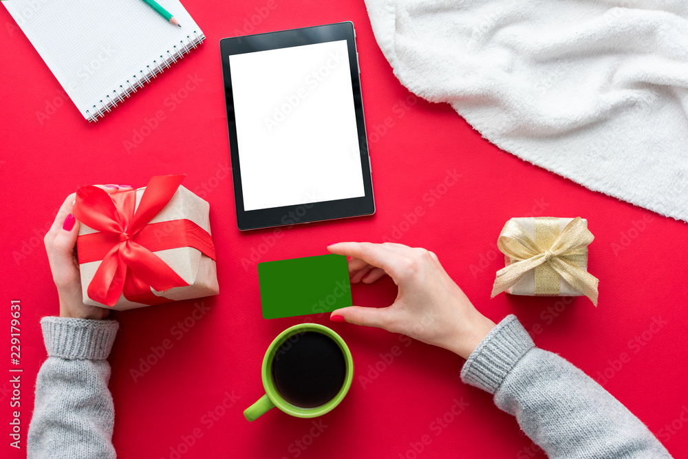 Female hands, woman holding a Business card and gift. Cup of coffee or tea, tablet pc, red table, gifts boxes for the holidays, background with copy space for advertisement, top view Female hands, woman holding a Business card and gift. Cup of coffee or tea, tablet pc, red table, gifts boxes for the holidays, background with copy space for advertisement, top view