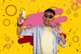 Selfie in sunglasses. Dark-haired teenager wearing striped shirt standing in front of colorful background making selfie in dark sunglasses