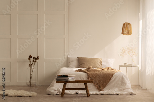 Beige blanket on the double bed in stylish wabi sabi bedroom of minimal style house, real photo with copy space on the empty wall photo