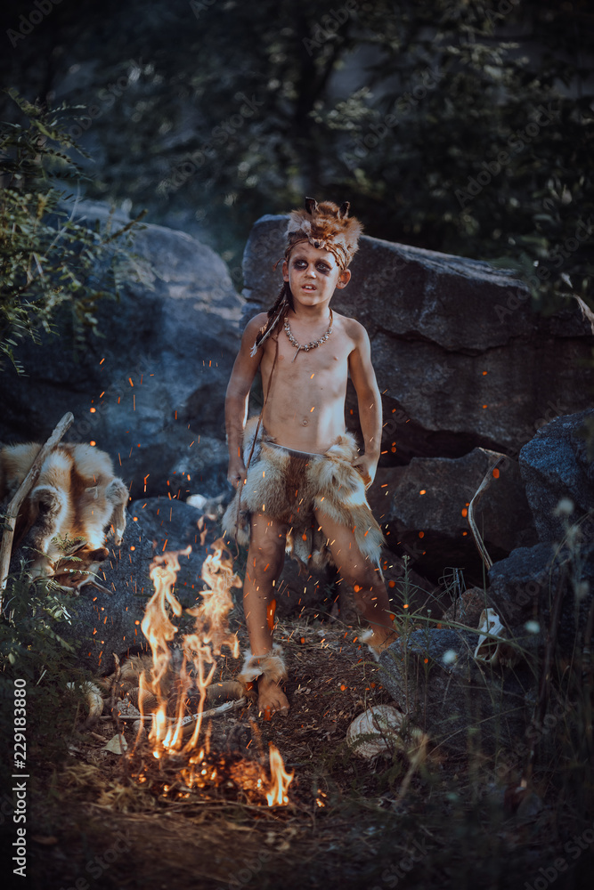 Caveman, manly boy at the fire. Scary young primitive boy outdoors near bonfire. Witch craft concept. Angry caveman, manly boy with horns near bonfire. Prehistoric tribal man outdoors on nature Caveman, manly boy at the fire. Scary young primitive boy outdoors near bonfire. Witch craft concept. Angry caveman, manly boy with horns near bonfire. Prehistoric tribal man outdoors on nature