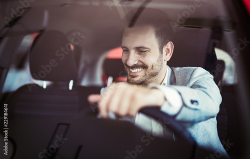 Fototapeta Attractive happy young man driving car and smiling