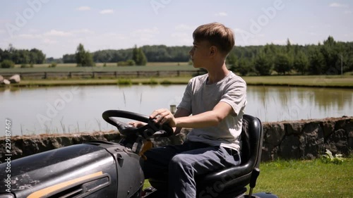 young boy driving lawn mower and taking care of his backyard, summer job