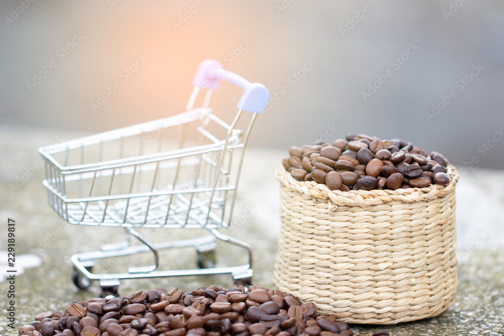 Coffee beans in brown basket with shopping cart on the table. The concept of seeds selection for beverage and distribution. Soft focus and copy space. Coffee beans in brown basket with shopping cart on the table. The concept of seeds selection for beverage and distribution. Soft focus and copy space.