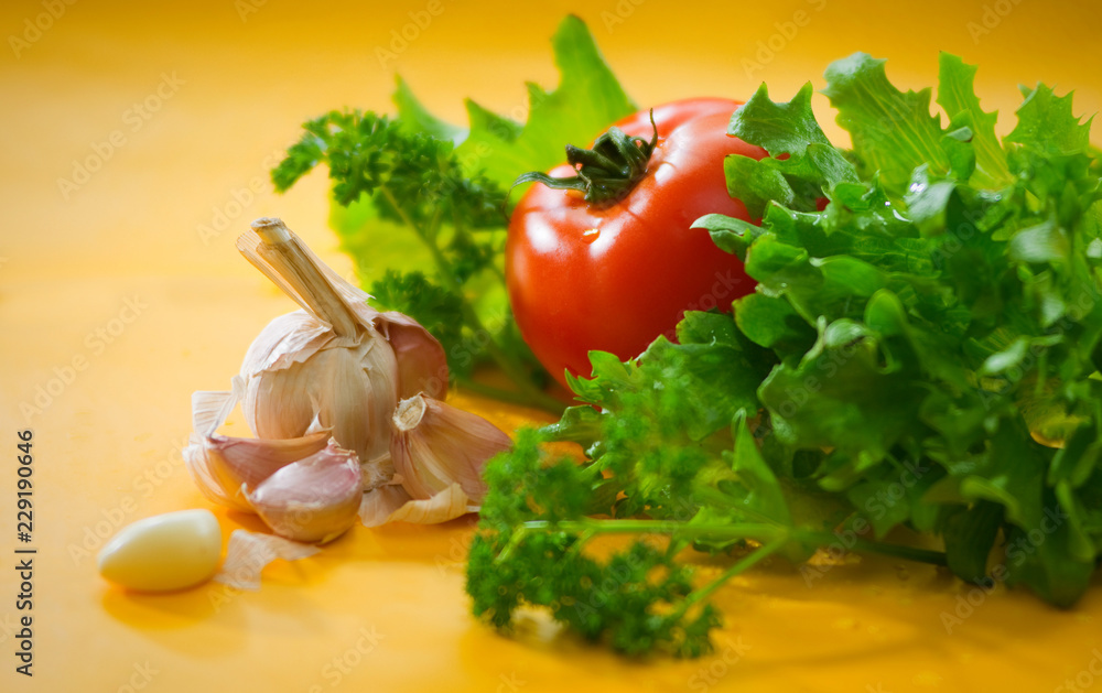 Овощи - помидор, чеснок, зеленый салат на желтом размытом фоне Vegetables - tomato, garlic, green salad on a yellow blurred background