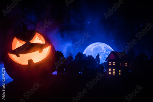 Horror view of Halloween pumpkin with scary smiling face. Head jack lantern with spooky building