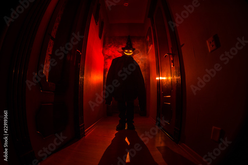 Halloween concept. Creepy silhouette in the dark corridor with pumpkin head. Toned light with fog on background. Selective focus