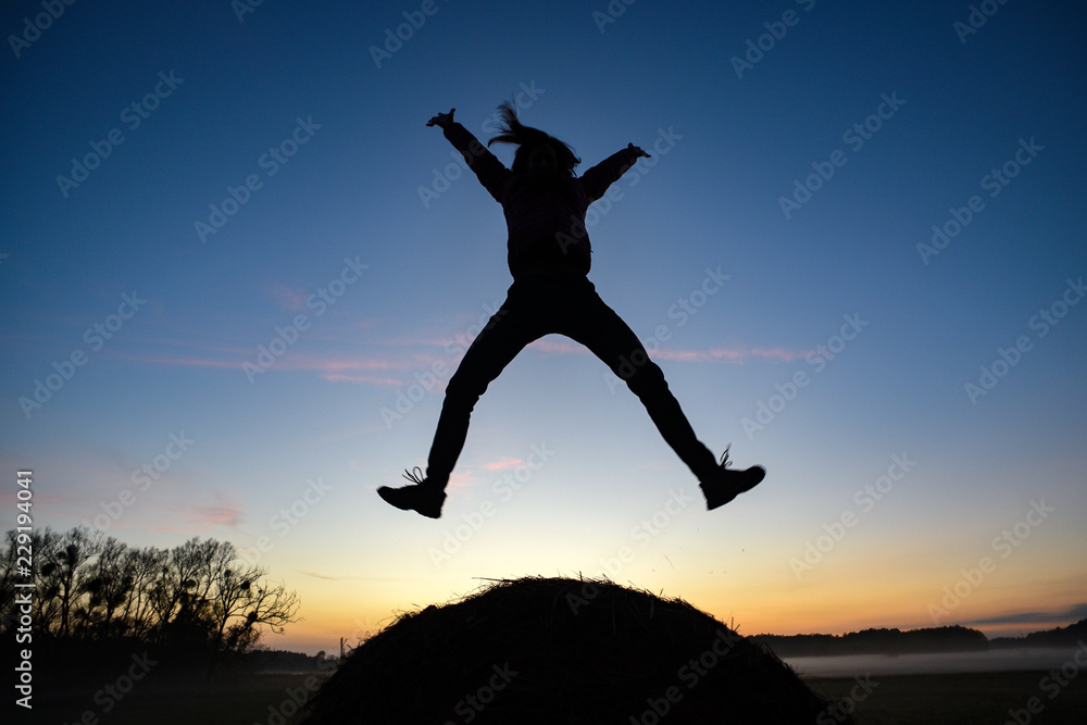 Happy woman jumping for joy on the background of the field and the setting sun.