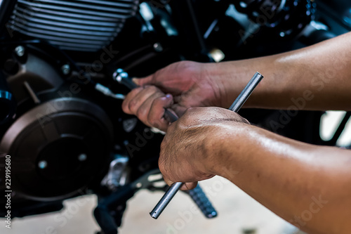 Image is close up. People holding hand are repairing a motorcycle Use a wrench and a screwdriver to work. Use the wrench to tighten the cylinder.