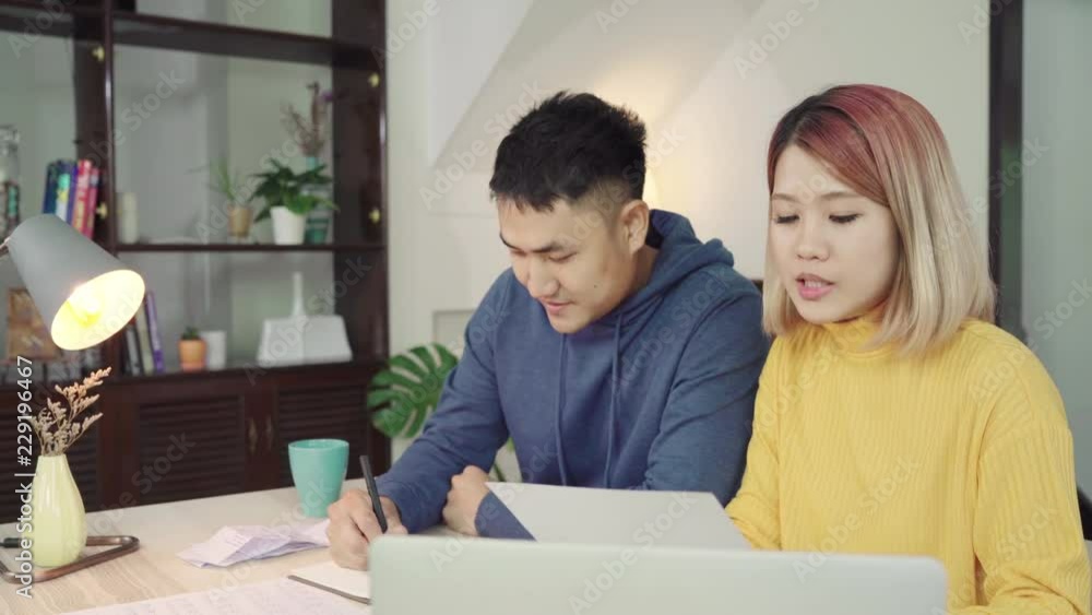 Young asian couple managing finances, reviewing their bank accounts using laptop computer and calculator at modern home. Woman and man doing paperwork together, paying taxes online on notebook pc. Young asian couple managing finances, reviewing their bank accounts using laptop computer and calculator at modern home. Woman and man doing paperwork together, paying taxes online on notebook pc.