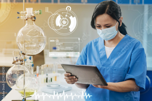 Looking at the screen. Attentive concentrated chemist holding a modern tablet and looking at the screen of it while working in the laboratory