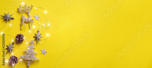Christmas and new year concept. Greeting banner with copyspace. Shiny silver deer, stars, fir-tree, garland, bokeh on yellow background. Top view, flat lay photo