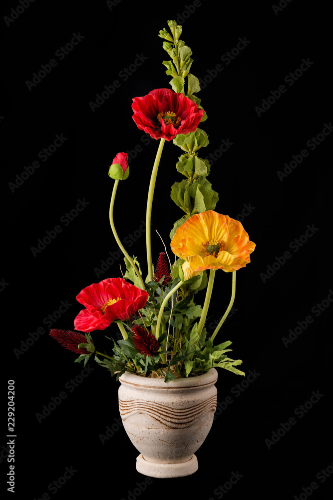 Floral arrangement from artificial poppy flowers in old ceramic flower pot.
