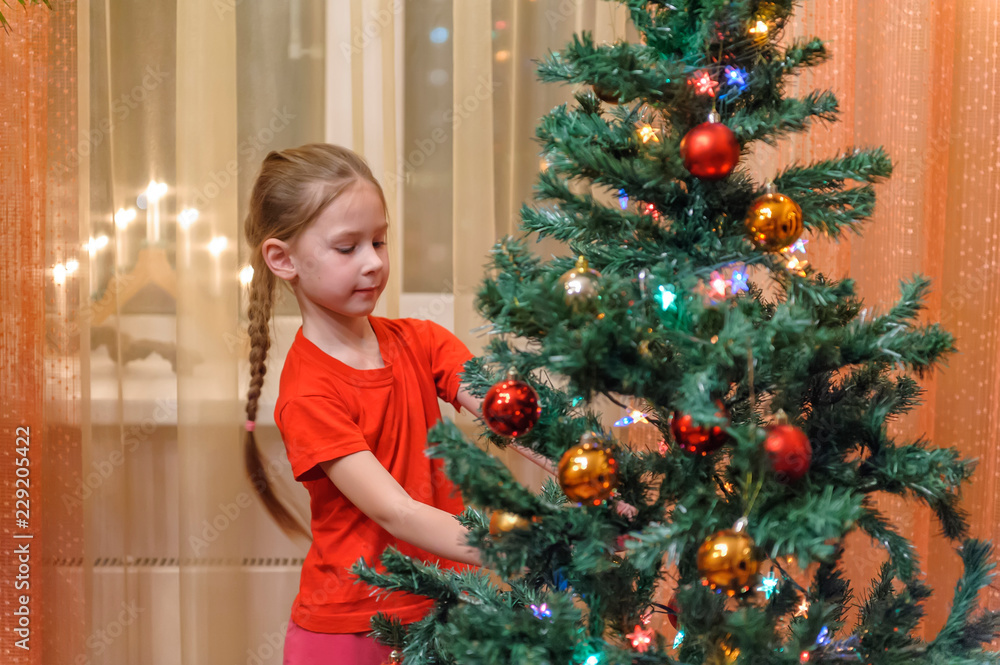 Adorable little girl decorating a Christmas tree with colorful glass baubles at home Adorable little girl decorating a Christmas tree with colorful glass baubles at home