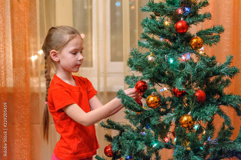Adorable little girl decorating a Christmas tree with colorful glass baubles at home