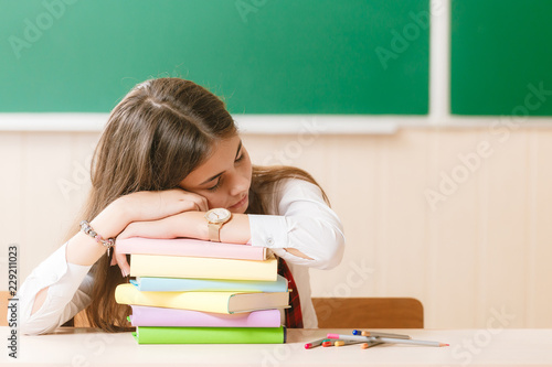 schoolgirl in school uniform sleeps on the books at the school desk