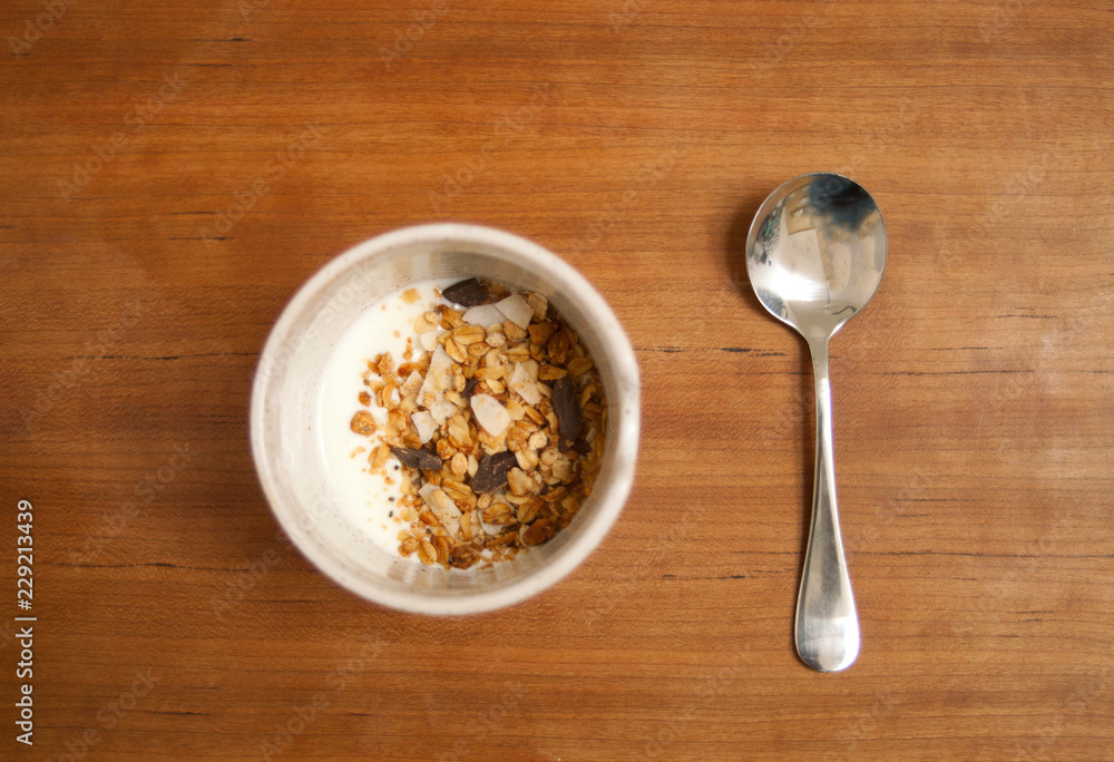 Overhead image of a spoon and bowl with yogurt and granola on a wooden table Overhead image of a spoon and bowl with yogurt and granola on a wooden table