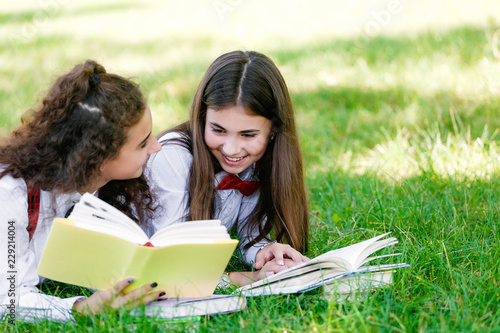 two funny schoolgirls are lying on the grass and reading books. Girls, girlfriends, sisters are taught lessons in nature