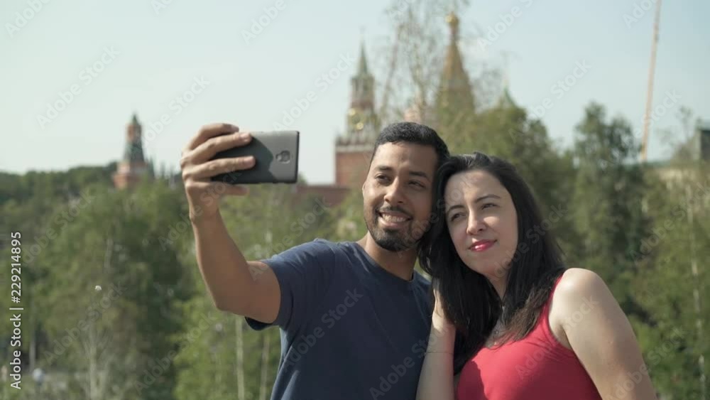 Cheerful hispanic man and his beautiful wife making a selfie with smartphone on sunny day in Moscow, Russia. Handheld slow motion medium shot Cheerful hispanic man and his beautiful wife making a selfie with smartphone on sunny day in Moscow, Russia. Handheld slow motion medium shot