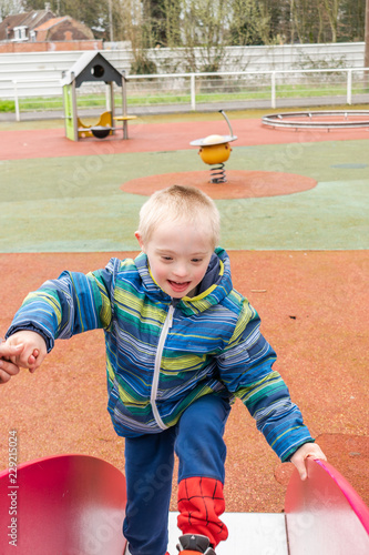Defect,childcare,medicine and people concept- young boy with a down syndrome who is playing in a playground.