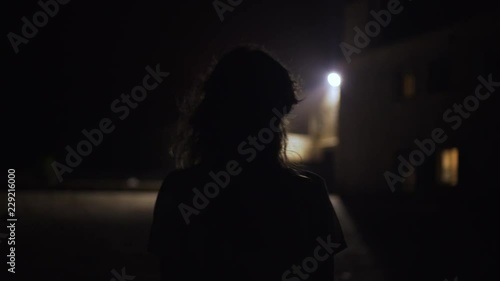 Silhouette of woman walks towards light at night in windy weather in Mallorca, Spain photo