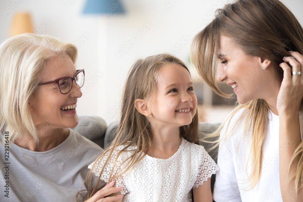 Smiling mother, daughter and grandmother sit on cozy couch at home having fun, three generations of women hugging enjoy spending time together, family of mom, granny and child relax indoors laughing Smiling mother, daughter and grandmother sit on cozy couch at home having fun, three generations of women hugging enjoy spending time together, family of mom, granny and child relax indoors laughing