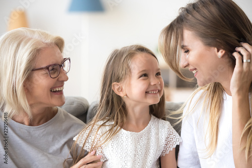 Smiling mother  daughter and grandmother sit on cozy couch at home having fun  three generations of women hugging enjoy spending time together  family of mom  granny and child relax indoors laughing