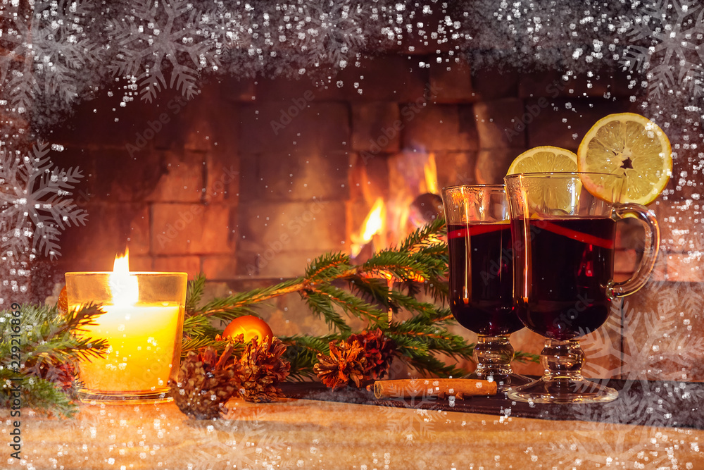 Two glasses with mulled wine, a candle, fir branches with decorations on a  wooden table against the background of a burning fireplace framed by  hoarfrost and snowflakes. Romantic christmas concept Stock Photo |