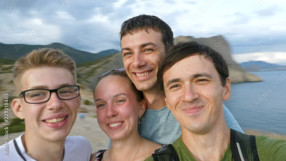 A group of young tourists makes a selfie video on nature, spinning around in a mountainous area near the sea. A group of young tourists makes a selfie video on nature, spinning around in a mountainous area near the sea.