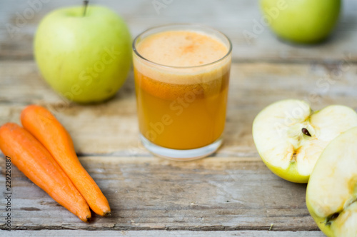 Homemade fresh squeezed apple and carrot healthy juice in a clear glass with apple and carrot on a side