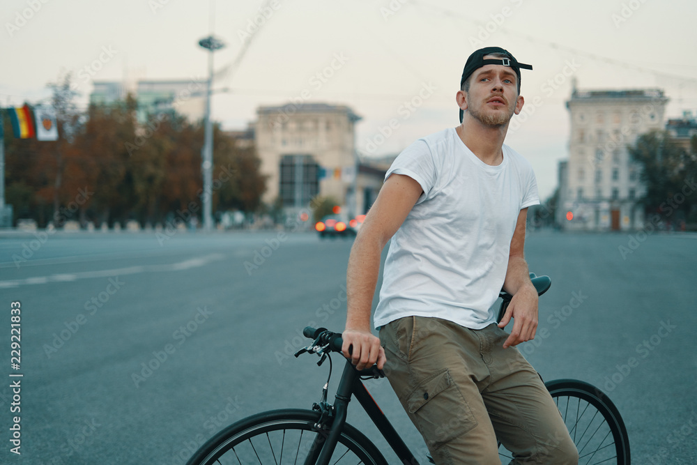 Fototapeta premium Outdoor portrait of a modern young man in the street, sitting on bike