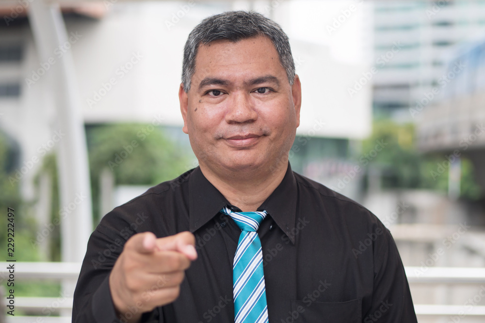 Fototapeta premium old business man pointing up at you, job recruit concept; portrait of confident, successful asian business man pointing finger or pointing hand at camera; 50s old south east asian man model