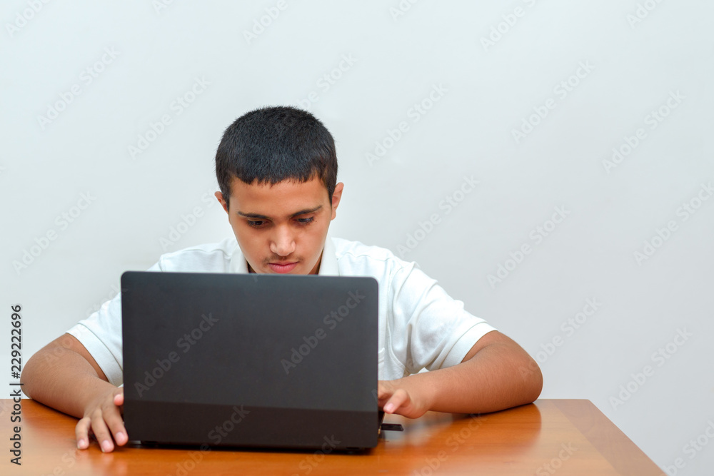 Teenager with laptop sitting at table and studying at home. Fashion portrait of teen black hair handsome boy in office. Young businessman using a laptop. Teenager with laptop sitting at table and studying at home. Fashion portrait of teen black hair handsome boy in office. Young businessman using a laptop.