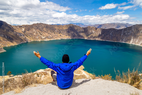 Homme voyageur bras en l'air Equateur lac coloré bleu nature montagne volcan Quilotoa